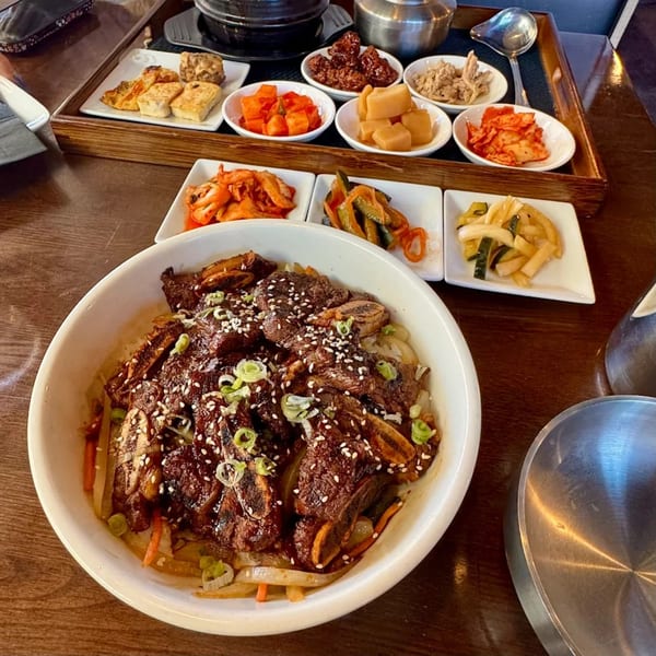 A Baekga Korean short rib dish with rice, topped with sesame seeds and green onions, surrounded by various banchan.