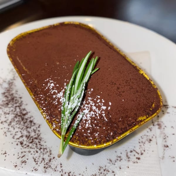 Baekga's tiramisu dessert, dusted with cocoa powder and powdered sugar, garnished with rosemary.