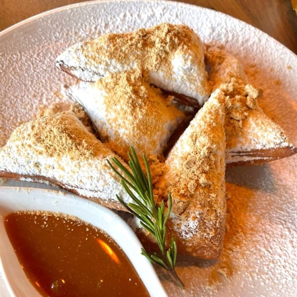 Baekga's Korean dessert features fried pastries dusted with powdered sugar and a brown crumble, served with caramel sauce.