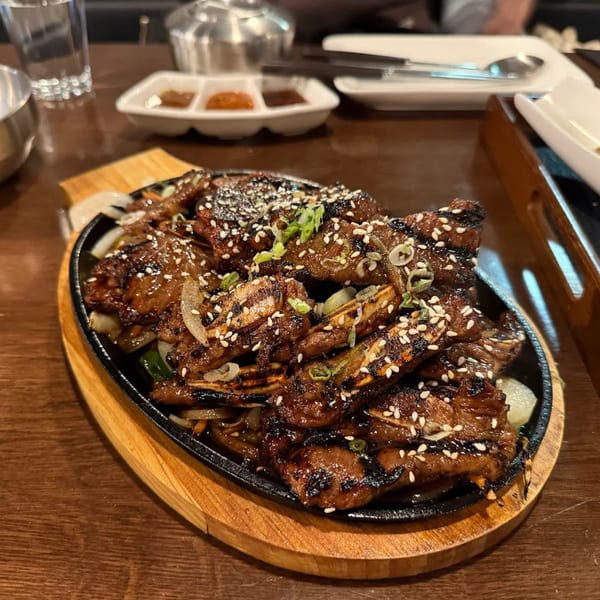 Sizzling Korean BBQ short ribs (galbi) with sesame seeds and green onions on a hot plate.